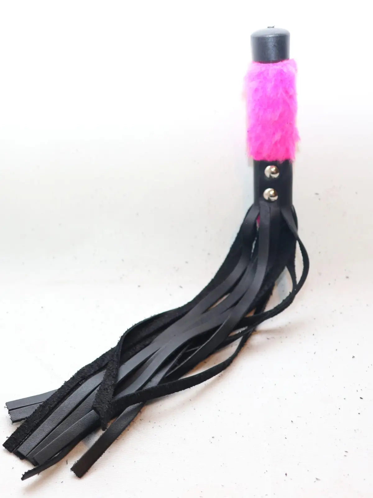 Lyhyt ruoska, jossa mustat nahkahapsut ja pinkki karvakahva – eroottinen ja näyttävä väline roolileikkeihin tai BDSM-käyttöön.