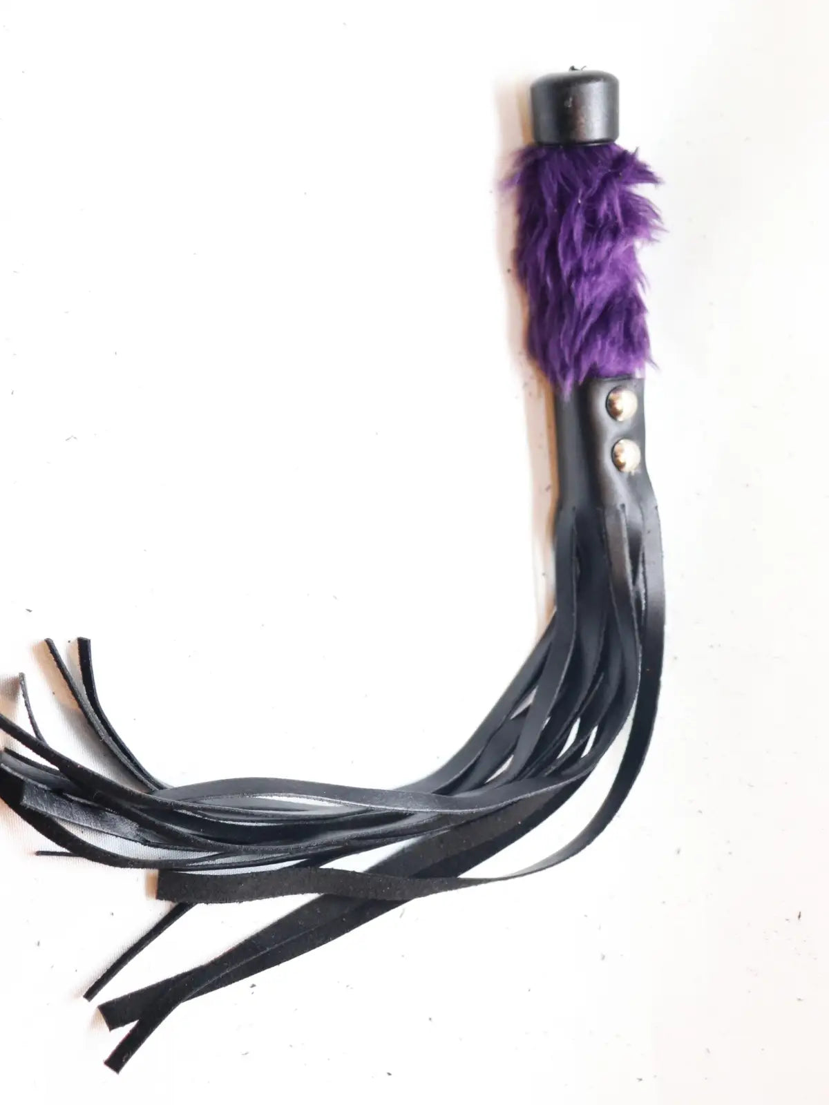 Lyhyt ruoska, jossa mustat nahkahapsut ja violetti karvakahva – eroottinen ja näyttävä väline roolileikkeihin tai BDSM-käyttöön